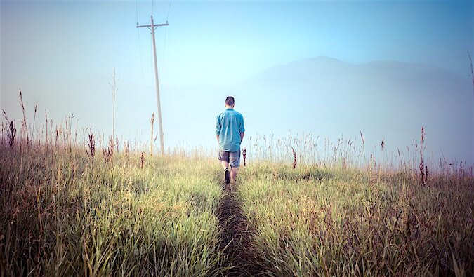 a man walking down a grass path in the countryside