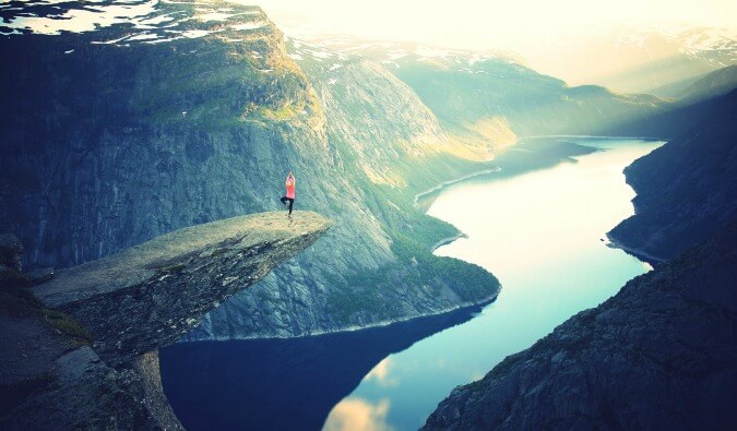 woman doing tree yoga pose on a cliff edge over a lake