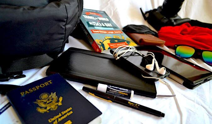 Passport, travel guide, headphones, pen, chapstick and other items laid out ready to pack for travel.