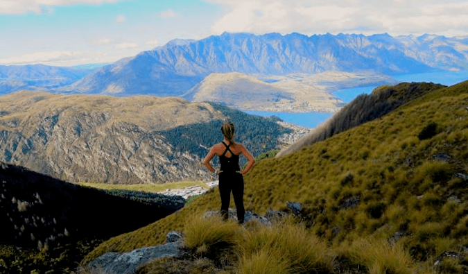 woman dressed in sportsware standing high in the mountains looking down at the view hands on hips