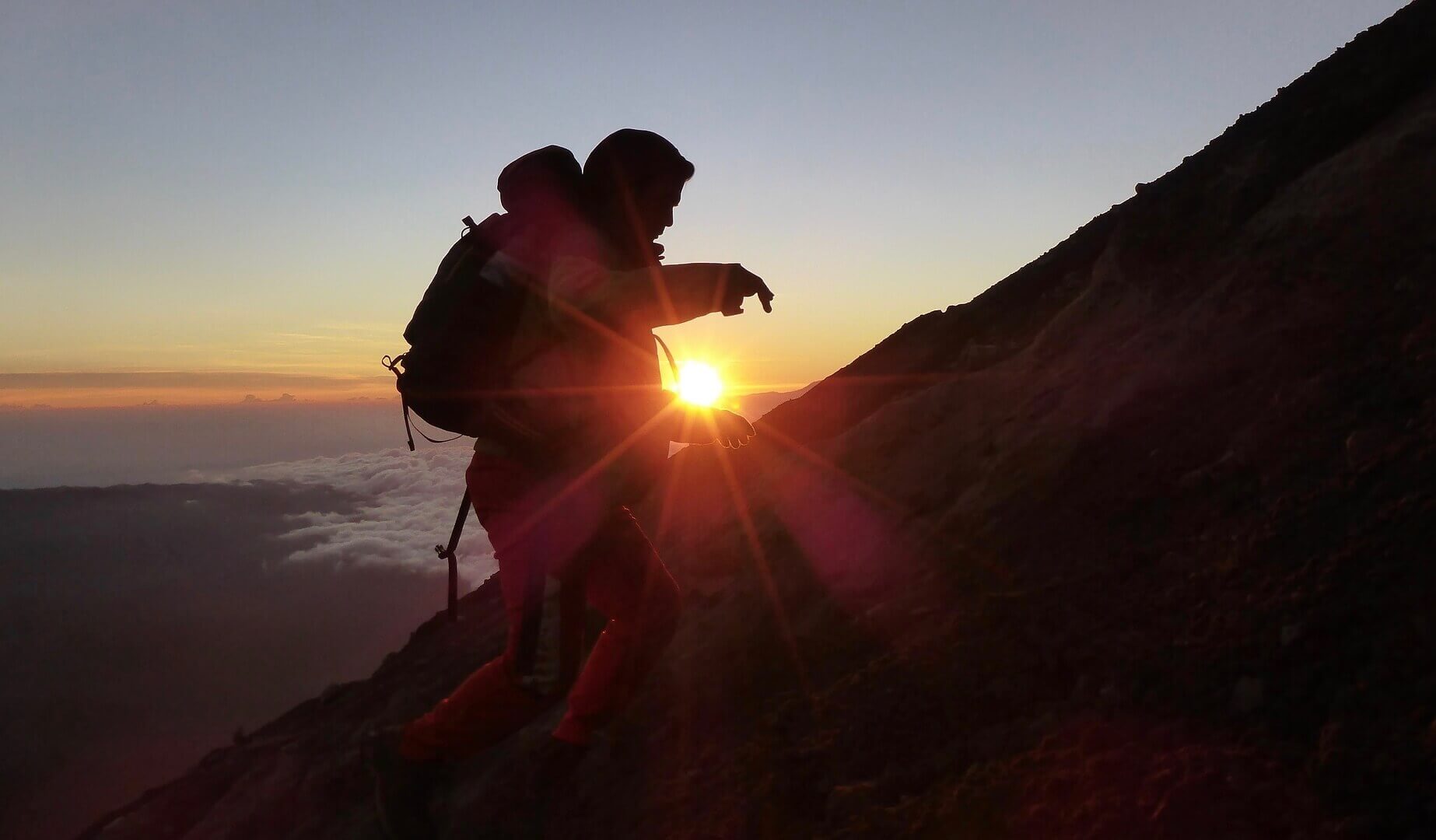 A guy hiking a mountain in sunset
