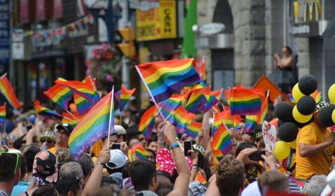 A crowd of people on a street at a pride event waving rainbow flags