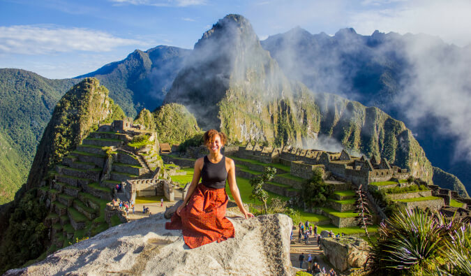 woman sat on a rock in foreground with Machu Picchu in he background